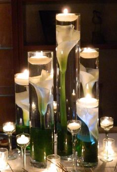 candles and flowers are arranged in glass vases on a table with lit candles around them