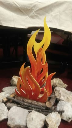 a fire sculpture sitting on top of a pile of rocks next to a white sheet