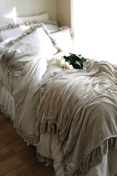 an unmade bed with white sheets and ruffled bedspread on the floor