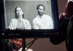 a man standing in front of a tv with two people on it's screen