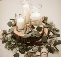 candles and greenery are arranged on a wood slice