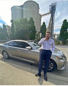 a man standing next to a silver car talking on a cell phone