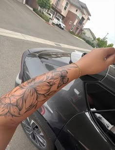 a person with a tattoo on their arm leaning out the window of a black car