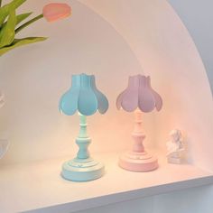 three colorful lamps sitting on top of a white shelf next to a potted plant