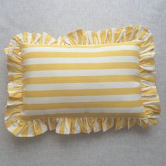 a yellow and white striped pillow with ruffles on the bottom, sitting on a gray surface