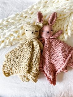 two crocheted stuffed animals laying next to each other on a white bed sheet