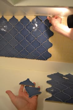 two hands are working on some tiles in a bathroom