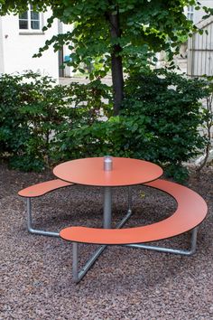 an orange table sitting in the middle of a gravel area next to trees and bushes