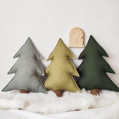 three christmas trees sitting on top of a white fur covered bed next to a wooden clock