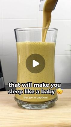 a glass filled with liquid sitting on top of a wooden table next to a blender