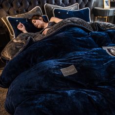 a woman laying on top of a blue comforter in a bed covered with pillows