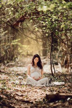 a pregnant woman is sitting in the woods with her belly up and looking at the camera