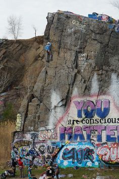 graffiti on the side of a mountain with people standing near by and looking at it