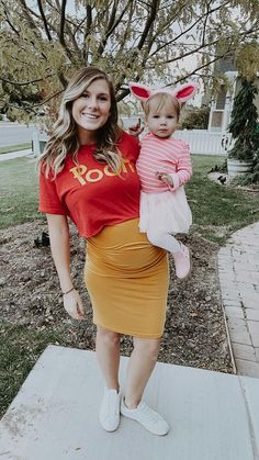 a woman in a red shirt and yellow skirt holding a toddler wearing bunny ears