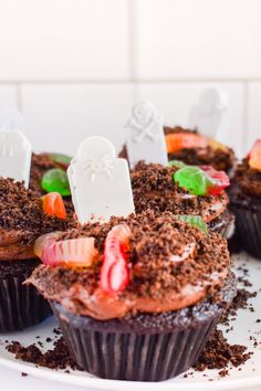 chocolate cupcakes decorated with candy and candies on a white plate in the shape of tombstones