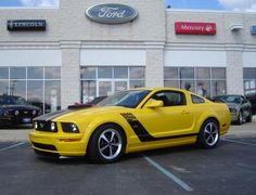 a yellow mustang parked in front of a ford dealership