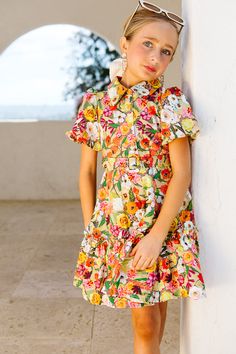 Be a ray of sunshine in our Mini Virginia Dress! This fun and flirty dress features a vibrant tan, orange, pink, white, and yellow floral print on lightweight cotton. With a high collar neckline, half-length puff sleeves, and a ruffled hem, you'll feel effortlessly chic. Plus, hidden pockets and a detachable belt add practicality and style. Ivy City Girls Mini Virginia Dress | Size: 12-18M Cotton Short Dresses, Thanksgiving Dress, A Ray Of Sunshine, Girls Holiday Dresses, Ray Of Sunshine, White Dress Party, Flirty Dresses, Holiday Party Dresses, Boys Romper