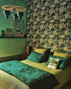 a bed with green sheets and pillows in front of a wallpapered headboard