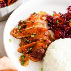 a white plate topped with chicken, rice and veggies next to a bowl of coleslaw