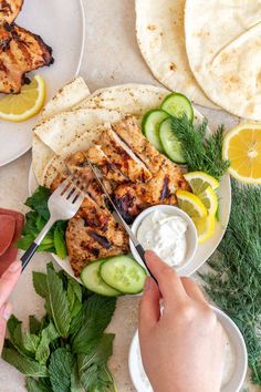 a plate with chicken, cucumbers, and pita bread on it next to some lemon wedges