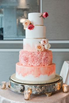 a three tiered wedding cake with pink and white flowers on the top is sitting on a silver platter