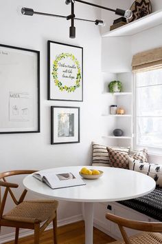 a white table and chairs in a room with pictures on the wall above it, along with a bowl of fruit