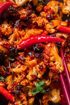 some red peppers and cauliflower are in a black bowl with chopsticks