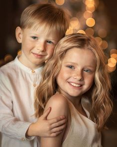 two young children posing for a photo in front of a christmas tree with lights behind them