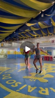 two women are dancing under an umbrella in a gym with yellow and blue stripes on the floor