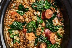 a crock pot filled with lentils, sausage and spinach in a brown sauce