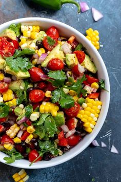 a bowl filled with corn, tomatoes and avocado on top of a table