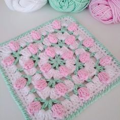 three balls of yarn sitting on top of a table next to a crocheted square