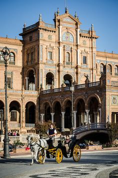 a horse drawn carriage parked in front of a large building with arches and pillars on the roof