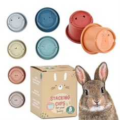 a rabbit is sitting next to several cups and boxes with bunny faces on them, all in different colors