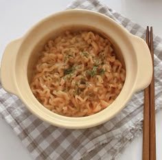 a bowl of noodles and chopsticks sitting on a napkin next to a fork