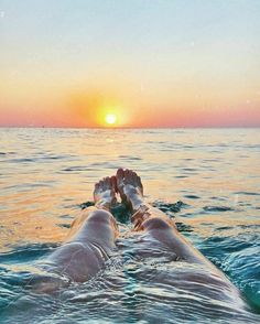 a person laying on their back in the ocean at sunset with their feet propped up