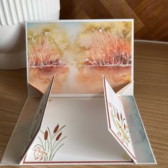 an open box with two cards inside on a wooden table next to a white vase