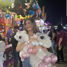 a woman holding two stuffed animals in her arms at an amusement park with other people