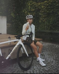 a woman sitting on a bench next to a bike eating an ice - cream cone