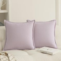 two purple pillows on a white couch with a remote control next to it and a book