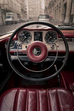 the interior of an old car with red leather seats and steering wheel, on a rainy day