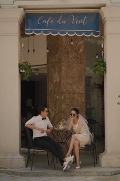 two people sitting at a table in front of a building with a sign that says cafe du ventt