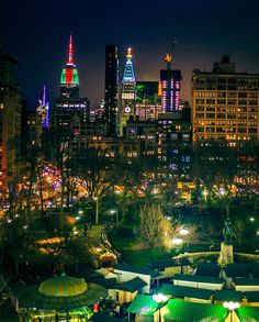 the city skyline is lit up at night with brightly colored lights on buildings and umbrellas