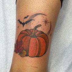 a small pumpkin tattoo on the arm with a bat and moon in the sky behind it