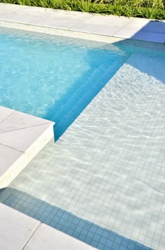 an empty swimming pool with steps leading up to the edge and grass in the background