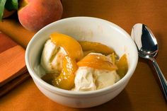 a bowl filled with ice cream and peaches on top of a table next to a spoon