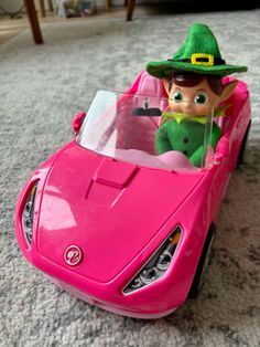 a pink toy car with a green hat on it's head sitting on the floor