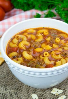 a white bowl filled with pasta and meat soup next to some bread on a table