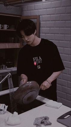 a man in a black t - shirt preparing food on top of a stovetop