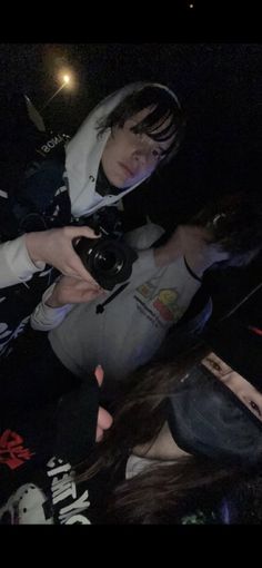 a woman taking a photo with her camera in the dark, while another person sits on the ground behind her